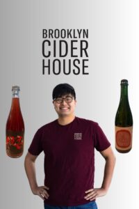 Richard Yi of Brooklyn Cider House standing between two bottles of cider beneath the Brooklyn Cider House logo.