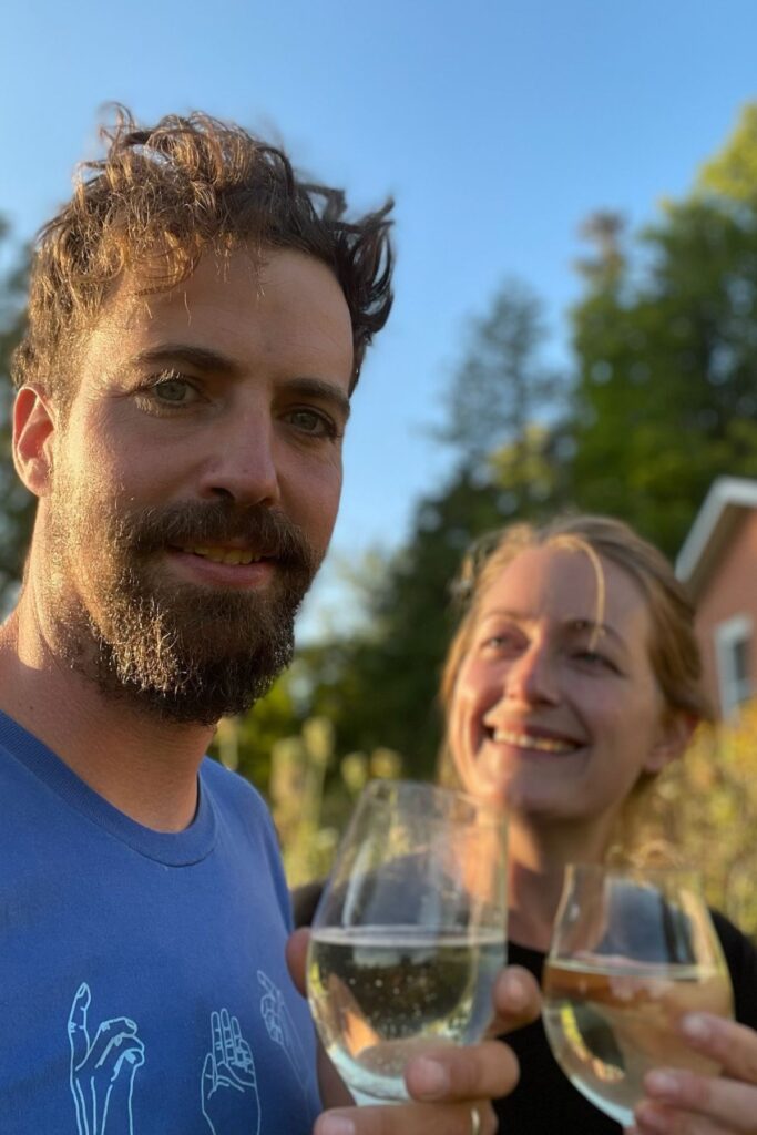Alastair Whitehead and Martha Lowry of Woodfolk Cider raise glasses of cider outdoors at their Ontario farm during golden hour.