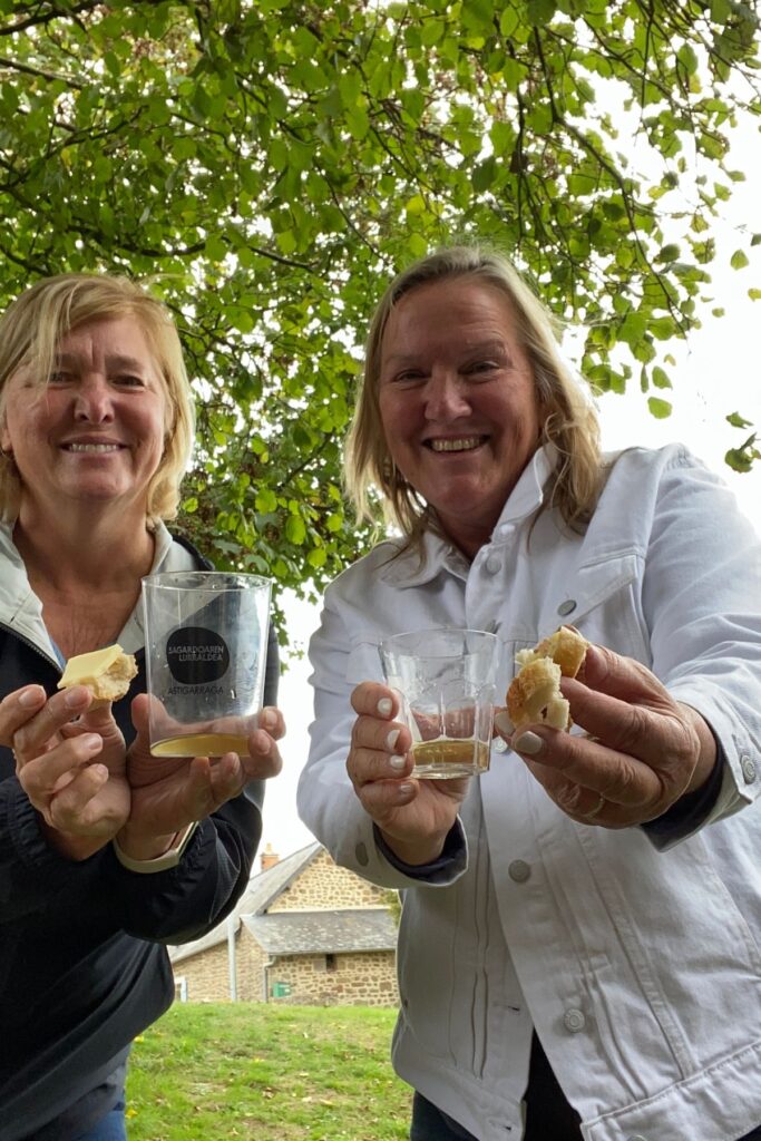 Two cider travelers enjoy local cider and bread outdoors during a cider tour in France.