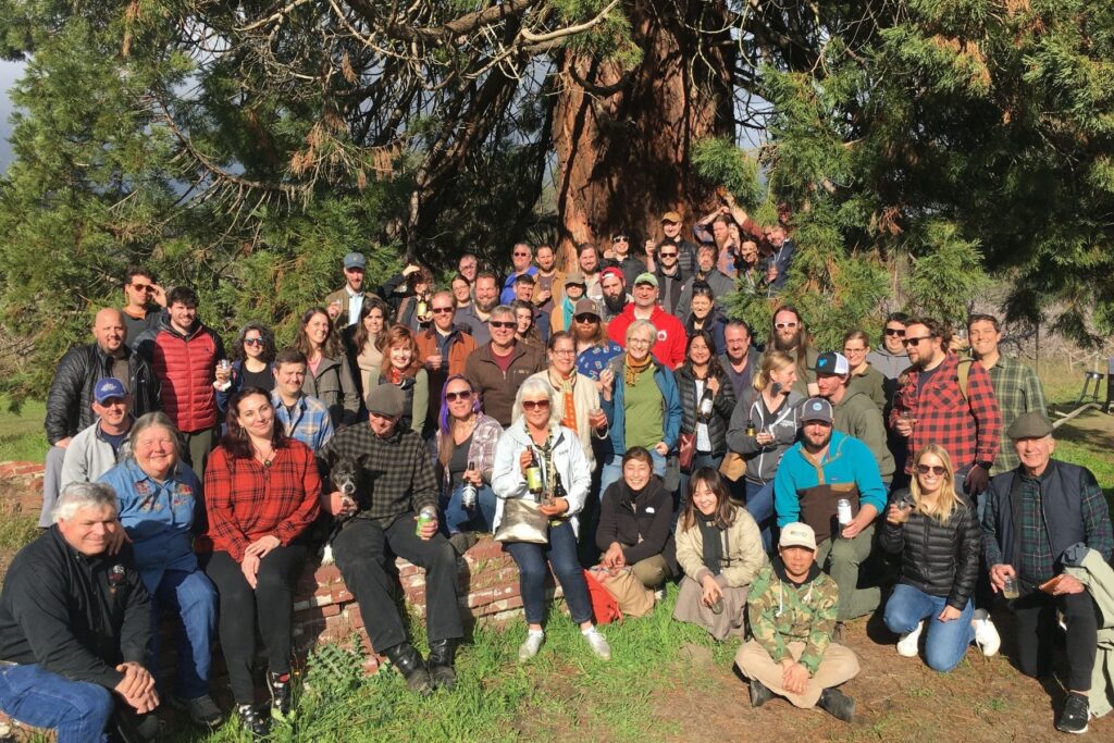Participants on a cider tour gather for a group photo beneath a large tree during a visit to an orchard in California's Pajaro Valley.