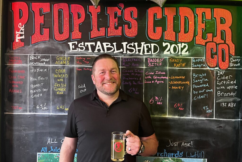Jason Lummen holds a mug of cider in front of The People's Cider Company tap board in Grand Rapids, Michigan.