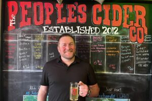 Jason Lummen holds a mug of cider in front of The People's Cider Company tap board in Grand Rapids, Michigan.