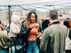 A festival attendee enjoys a cider doughnut while sampling hard cider at a CiderFeast event, highlighting the food, cider, and community experience.